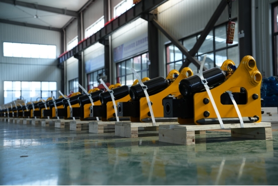 Rows of yellow hydraulic rock breakers neatly stacked in an industrial factory