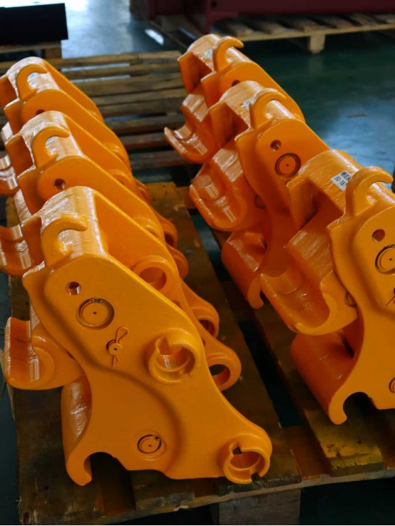 Multiple orange excavator quick hitch couplers stacked on wooden pallets
