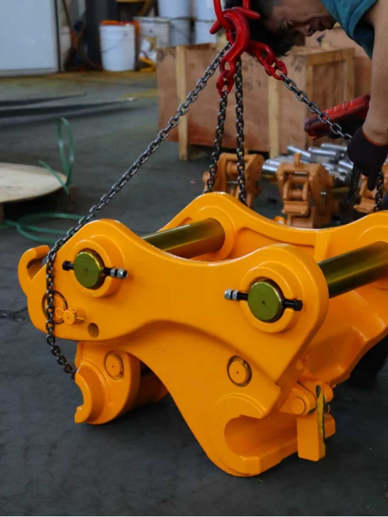 Yellow hydraulic quick coupler for excavator being lifted in factory